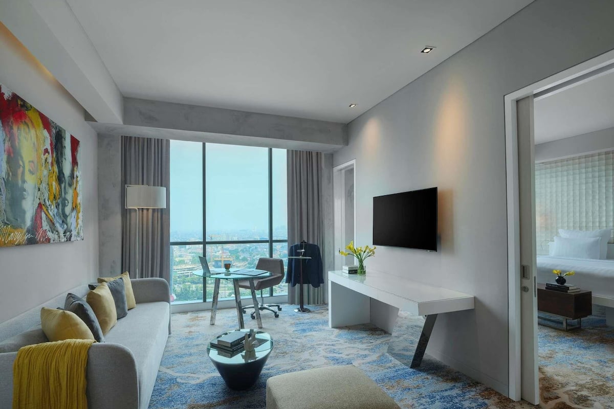 Une chambre d’hôtel moderne dotée d’une grande fenêtre, d’un canapé, d’un bureau, d’une télévision et offrant une vue sur le paysage urbain.
