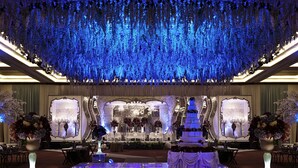 A grand hall with a tiered stage, floral arrangements, and a chandelier.