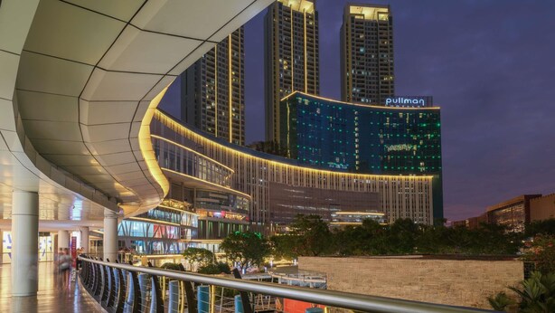 A modern hotel with a curved facade, a prominent 'Pullman' sign, and a view of surrounding high-rise buildings.