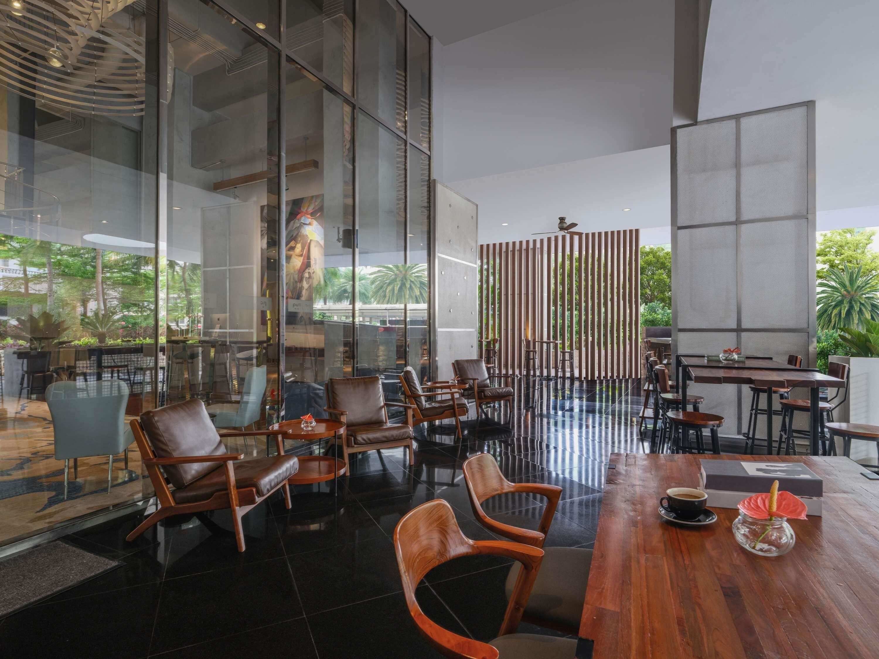 A modern indoor space with glass walls, wooden furniture, and a view of greenery outside.