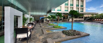 A hotel pool area with outdoor seating and a modern building in the background.