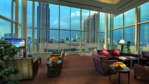 A modern hotel room with large windows offering a city view, a flat-screen TV, comfortable seating, and a small table with flowers. - Furama Bukit Bintang (Kuala Lumpur)