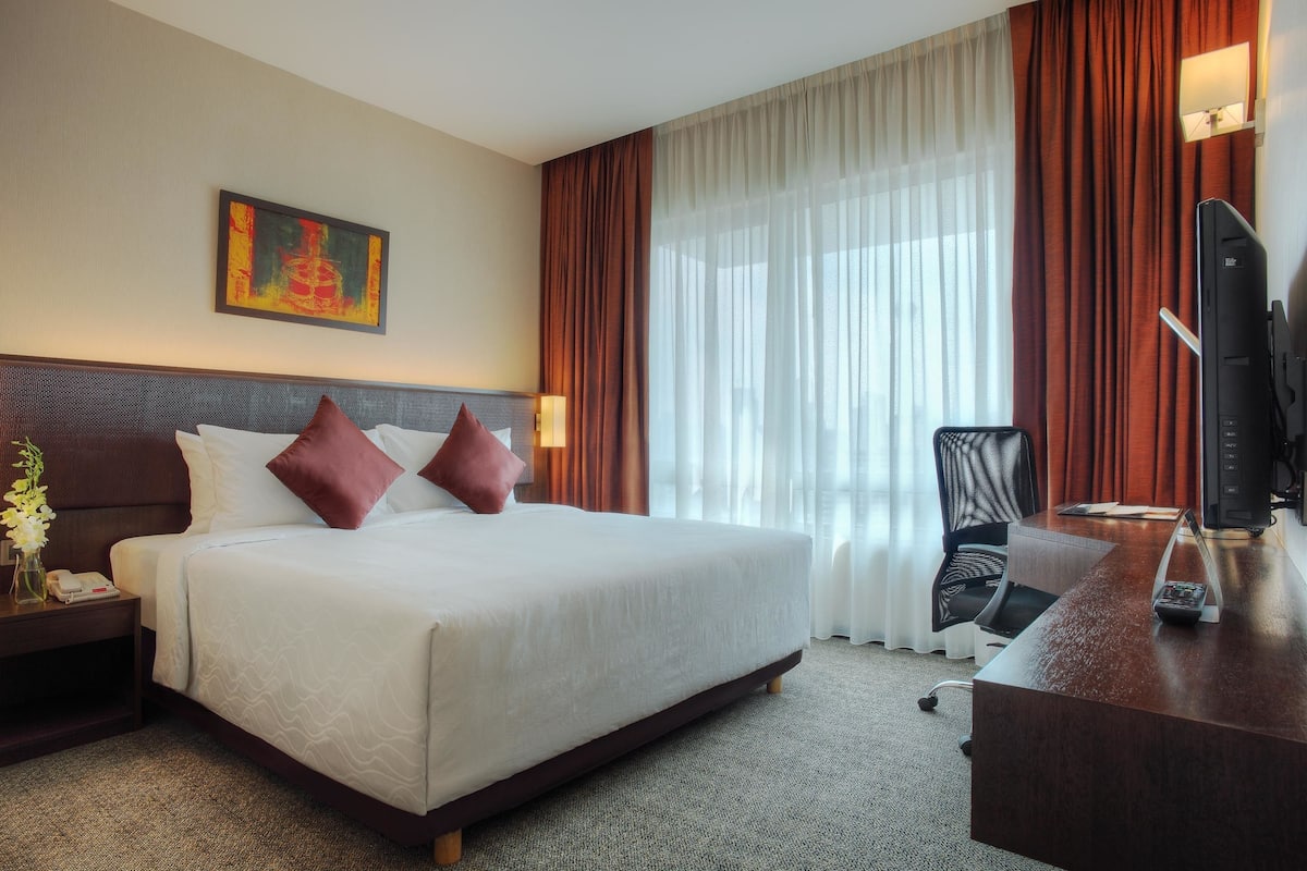 A hotel room with a large bed, a desk with a computer, a chair, a TV, and a painting on the wall.