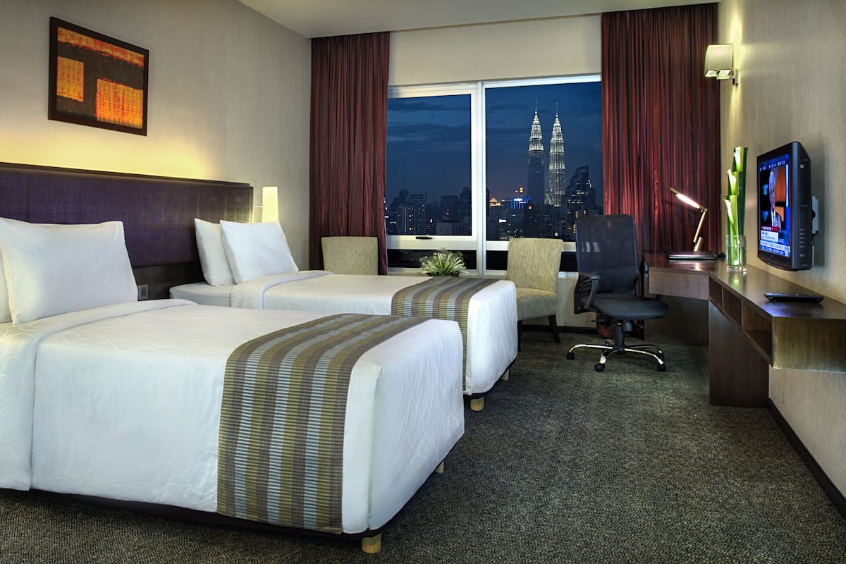 A hotel room with two beds, a desk, a TV, and a view of the cityscape.