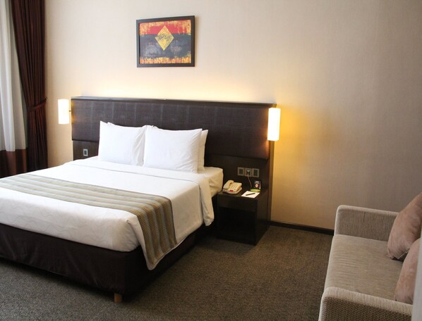 A hotel room with a large bed, a nightstand with a phone, and a chair.
