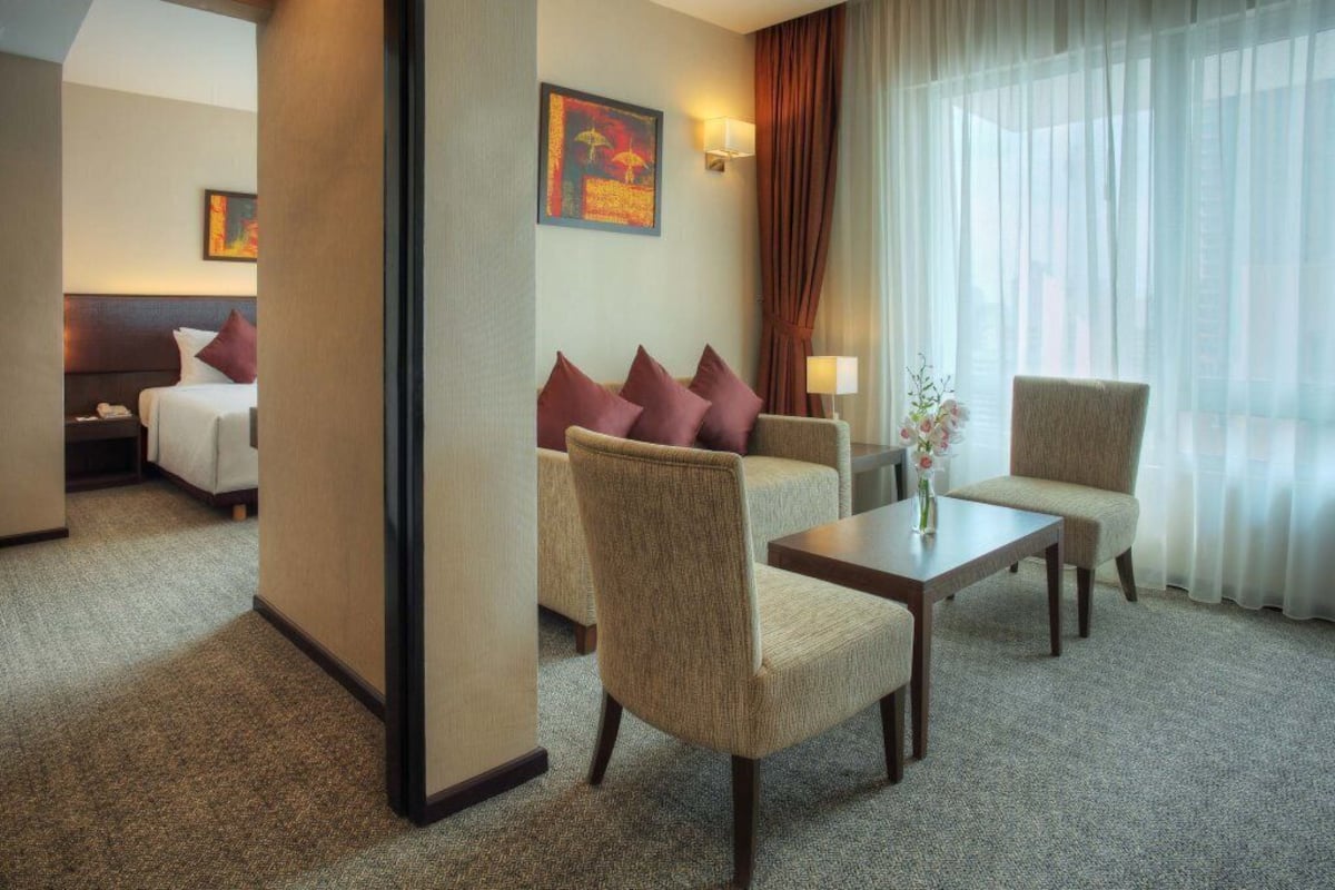 A hotel room with a bed, two armchairs, a small table, and a window with sheer curtains.