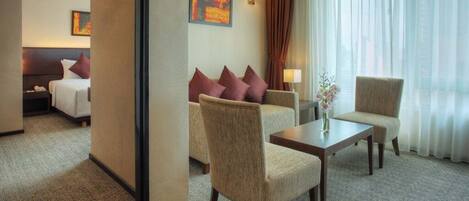 A hotel room with a bed, two armchairs, a small table, and a window with sheer curtains.