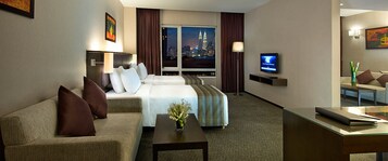 A hotel room with a bed, a sofa, a TV, and a view of a cityscape.
