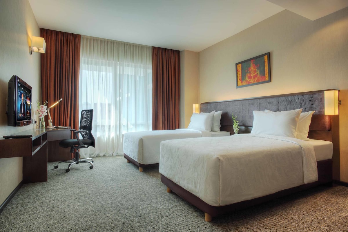 A hotel room with two beds, a desk, a chair, and a television.