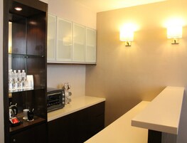 A hotel room with a minibar, a coffee machine, and two wall-mounted lights.