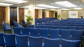 Un salón de conferencias con filas de sillas azules, un escenario con un atril y un cartel que dice "FURAMA".
