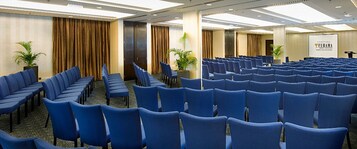 Un salón de conferencias con filas de sillas azules, un escenario con un atril y un cartel que dice "FURAMA".