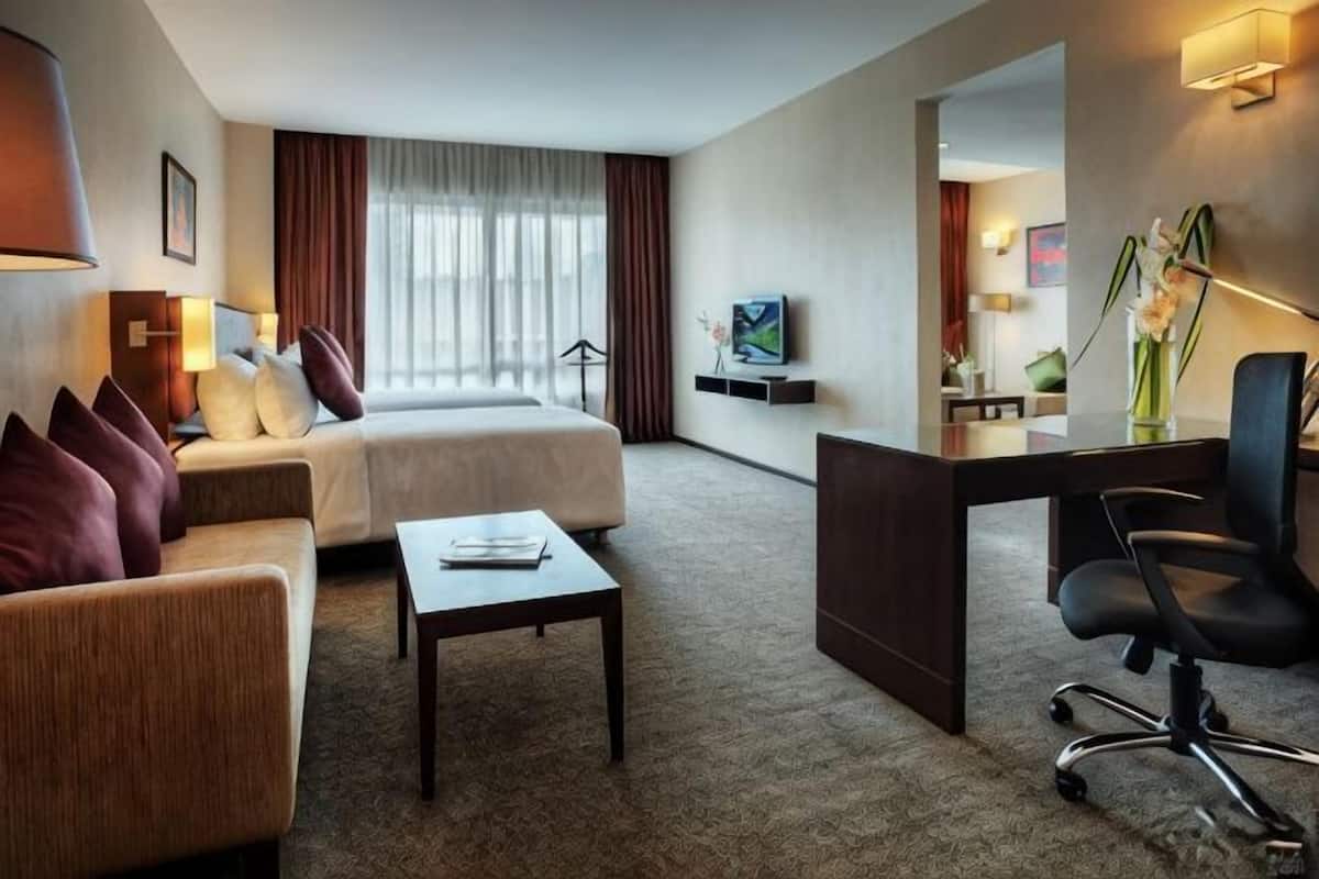A hotel room with a bed, a desk, a chair, a sofa, and a TV.