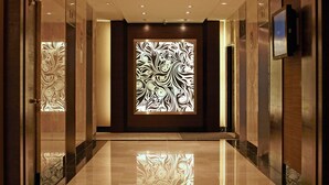 A hallway with a reflective floor, a decorative wall panel, and an elevator on the right. - Furama Bukit Bintang (Kuala Lumpur)