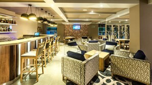 A bar area with wooden chairs and sofas, a television screen, and a bar counter with bottles.