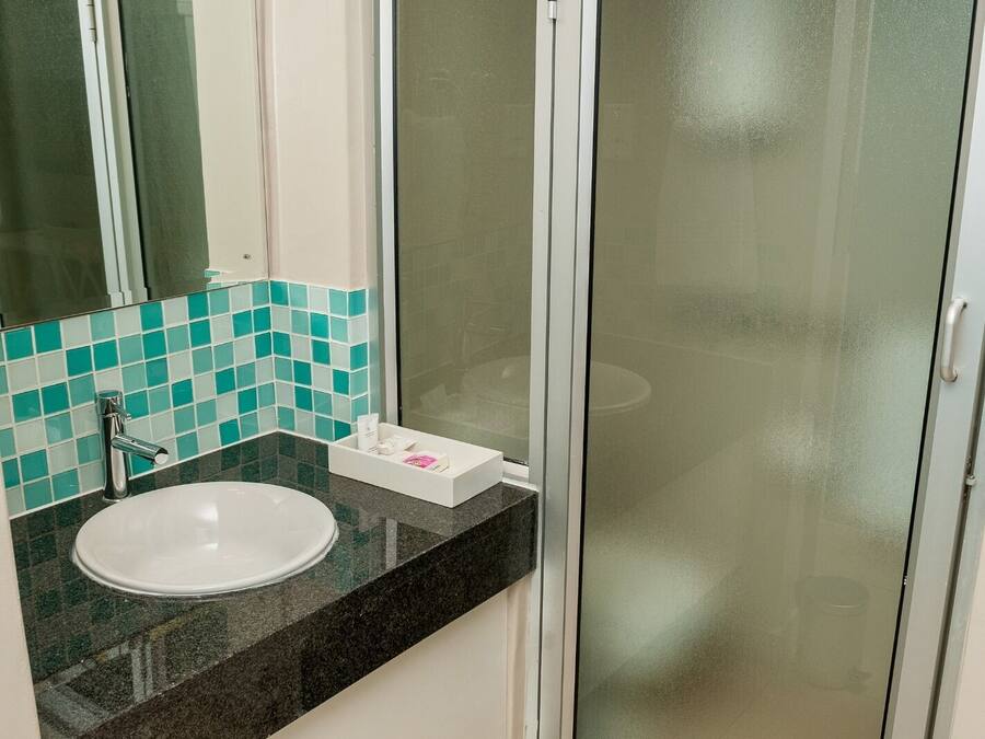 Un baño con lavamanos blanco, un espejo y una cabina de ducha con mampara de cristal.