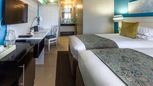 A hotel room with a bed, a desk, a chair, a TV, and a kitchenette.