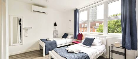 A modern bedroom with two beds, a window with curtains, a bedside table, and an air conditioning unit.