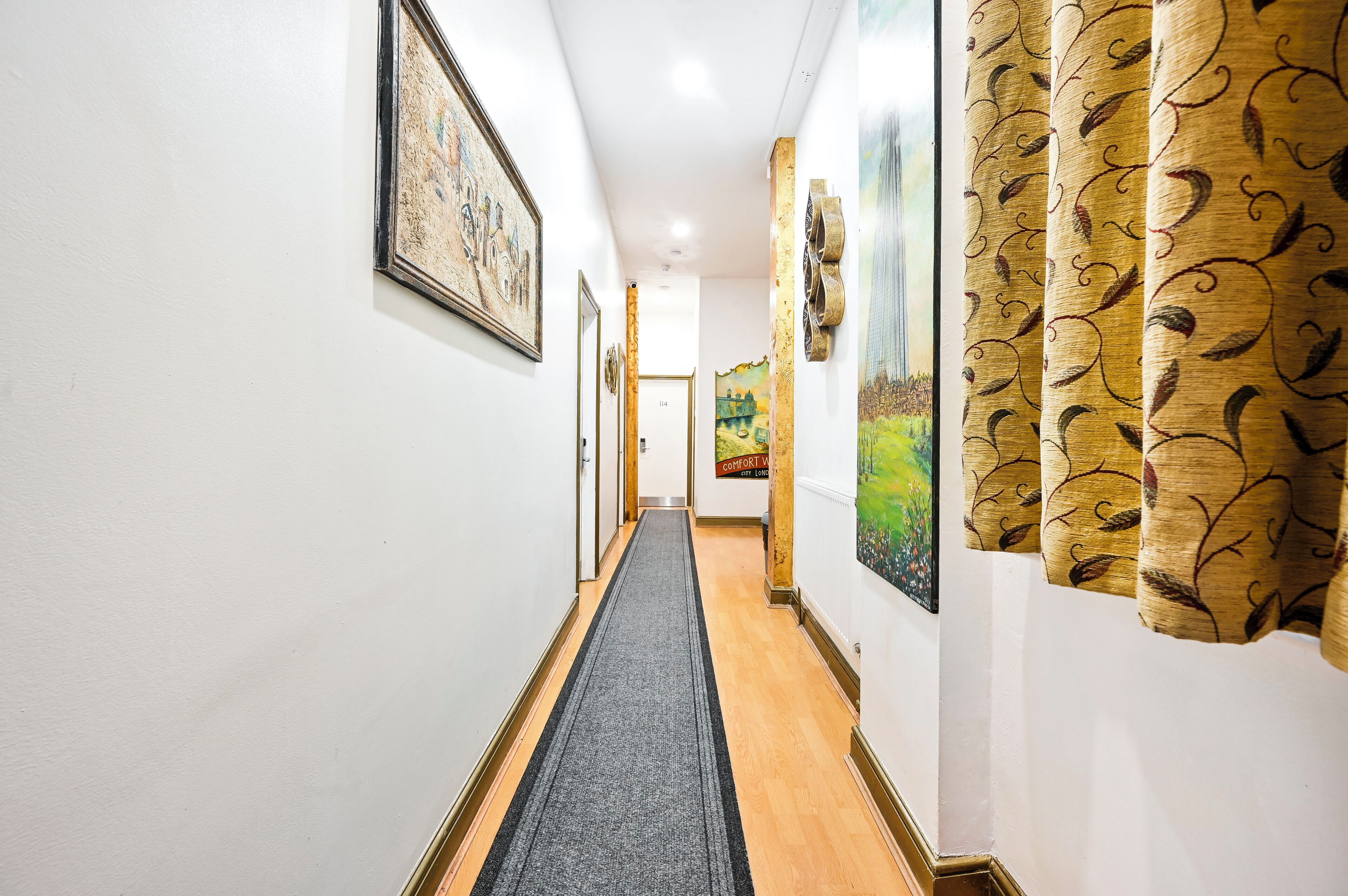 A hallway with framed artwork on the walls, a carpeted floor, and a door at the end.
