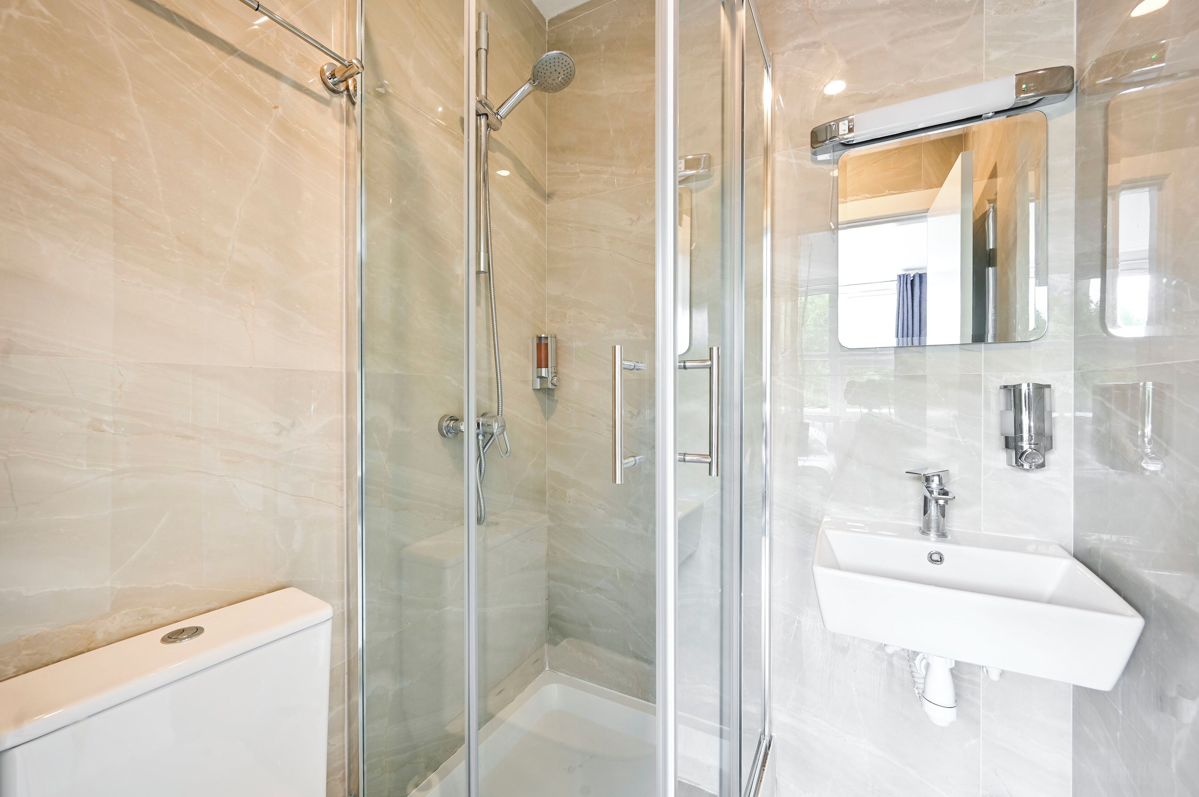 Un bany modern amb dutxa de vidre, un lavabo blanc i un mirall a sobre.