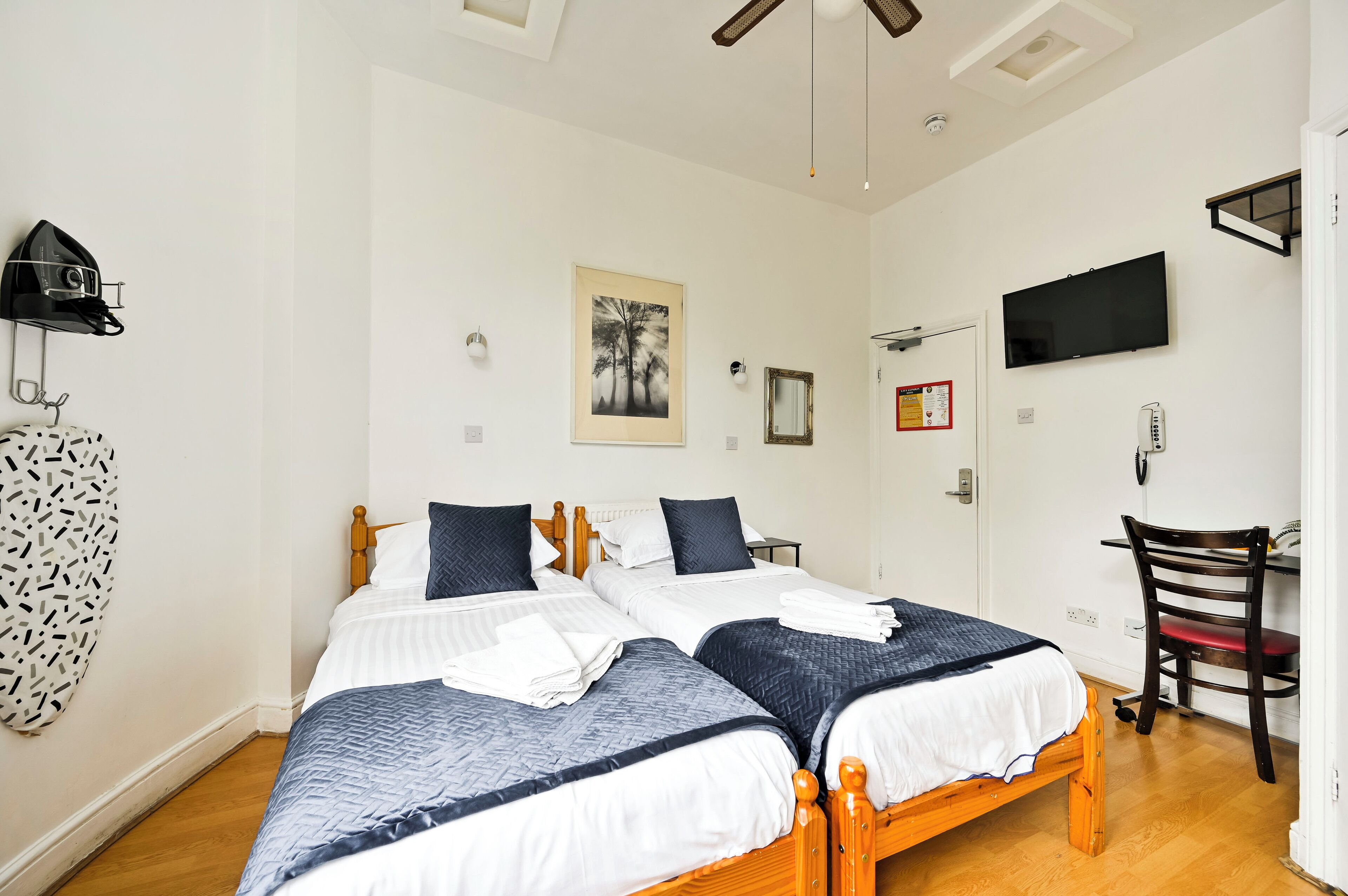 Una habitación con dos camas, un escritorio, una silla, un televisor y un ventilador de techo.
