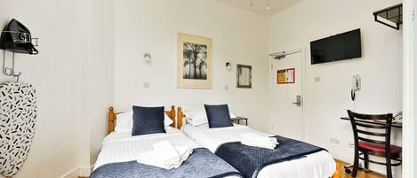 Une chambre avec deux lits, un bureau, une chaise, une télévision et un ventilateur de plafond.