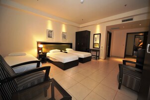 Habitación de hotel con cama doble, dos camas individuales, escritorio, silla, armario y espejo.