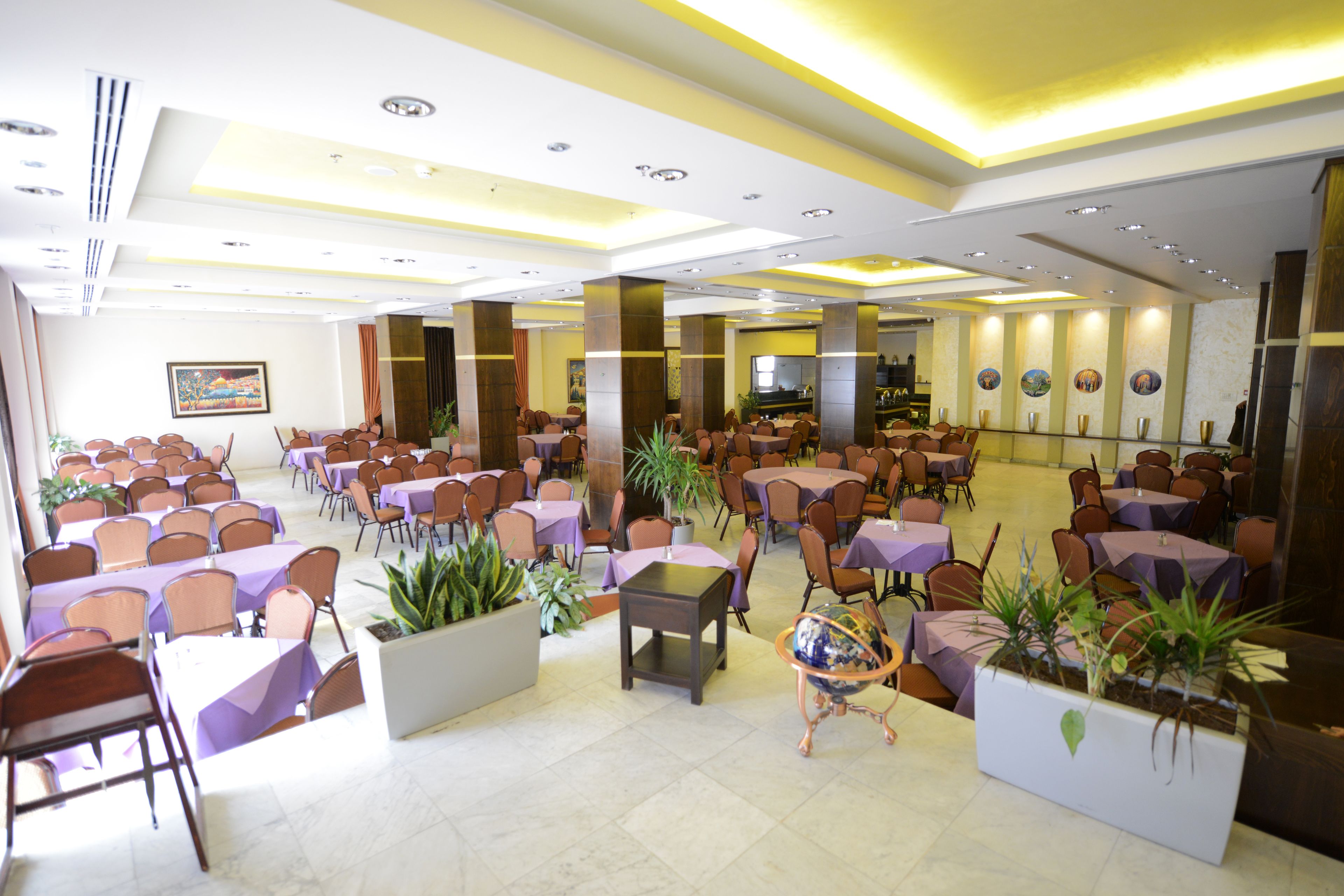 Eine geräumige Hotelhalle mit mehreren Essbereichen, großen Säulen und Pflanzentöpfen.