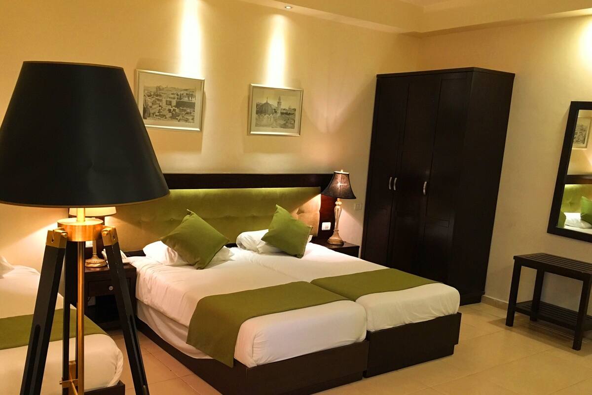 A hotel room with a large bed, two bedside tables, a wardrobe, and two wall-mounted lamps.