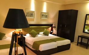Une chambre d’hôtel avec un grand lit, deux tables de chevet, une armoire et deux lampes fixées au mur.
