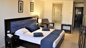 Une chambre d’hôtel avec un grand lit, une table de chevet avec un téléphone, une chaise et un bureau avec une lampe.