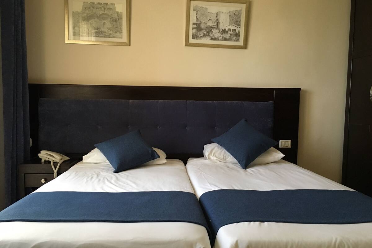 A double bed with two pillows, a bedside phone, and two framed pictures on the wall.