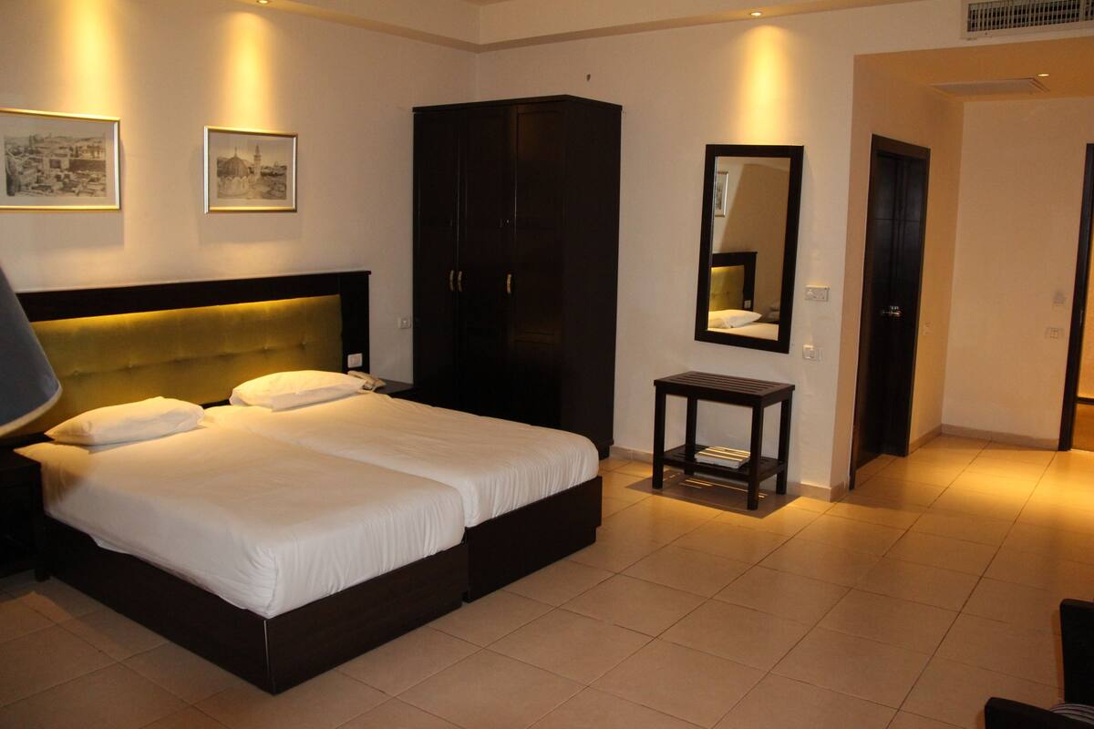 A hotel room with a large bed, a wardrobe, a bedside table, and framed pictures on the wall.