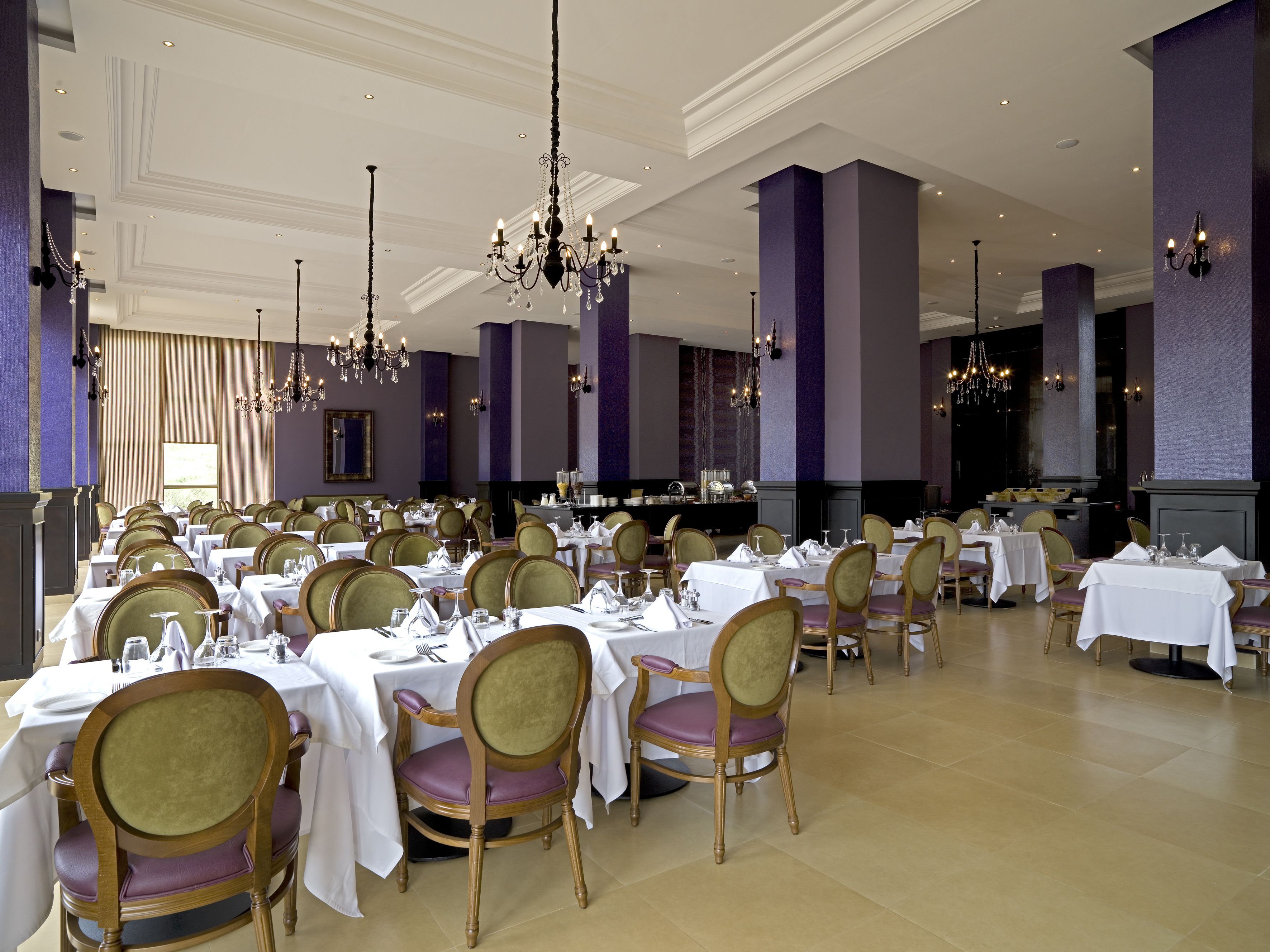 A formal dining room with multiple tables set for service, elegant chandeliers, and a classic interior design.