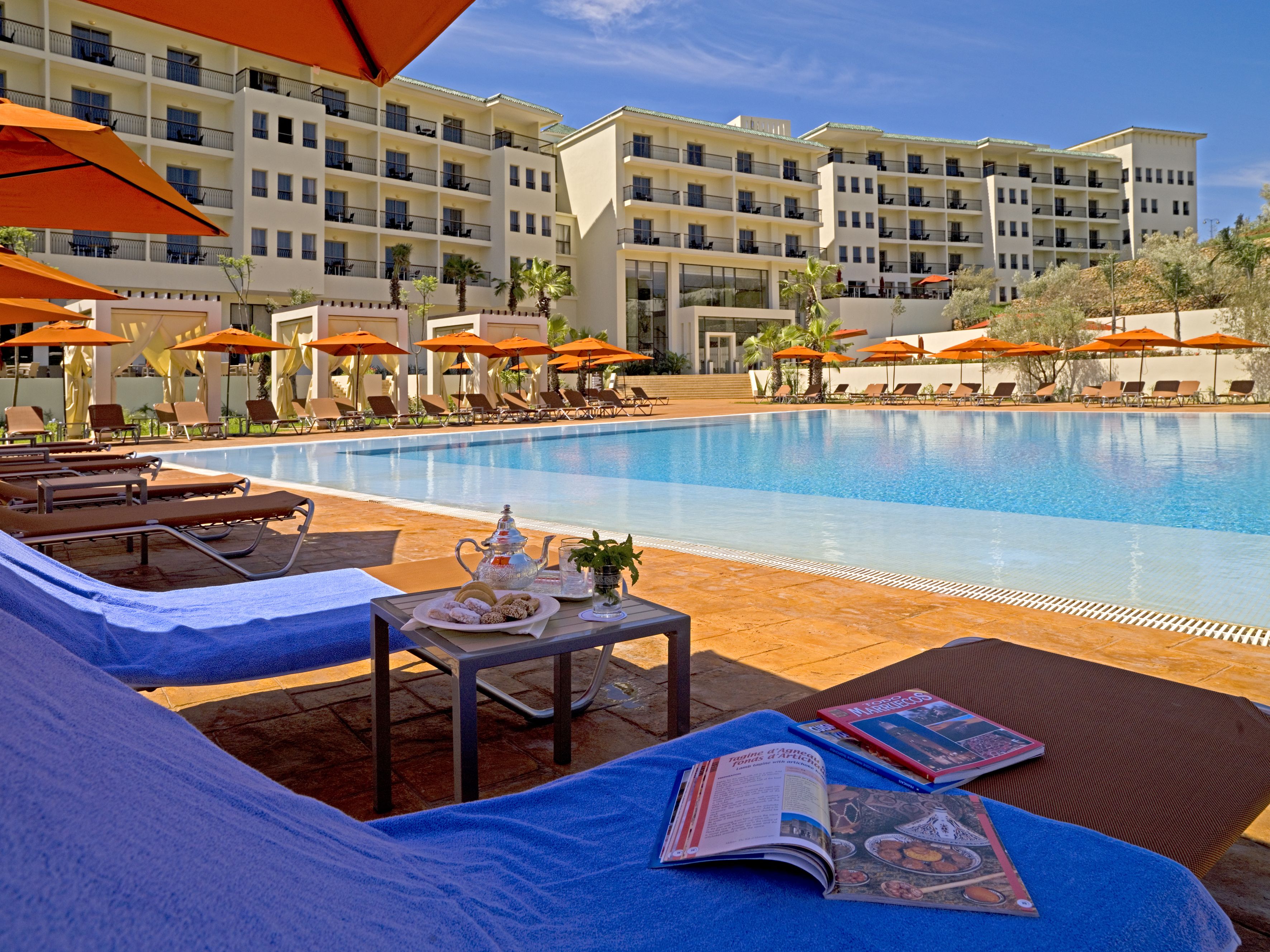 A poolside area with lounge chairs, umbrellas, and a table with a book and a teapot.