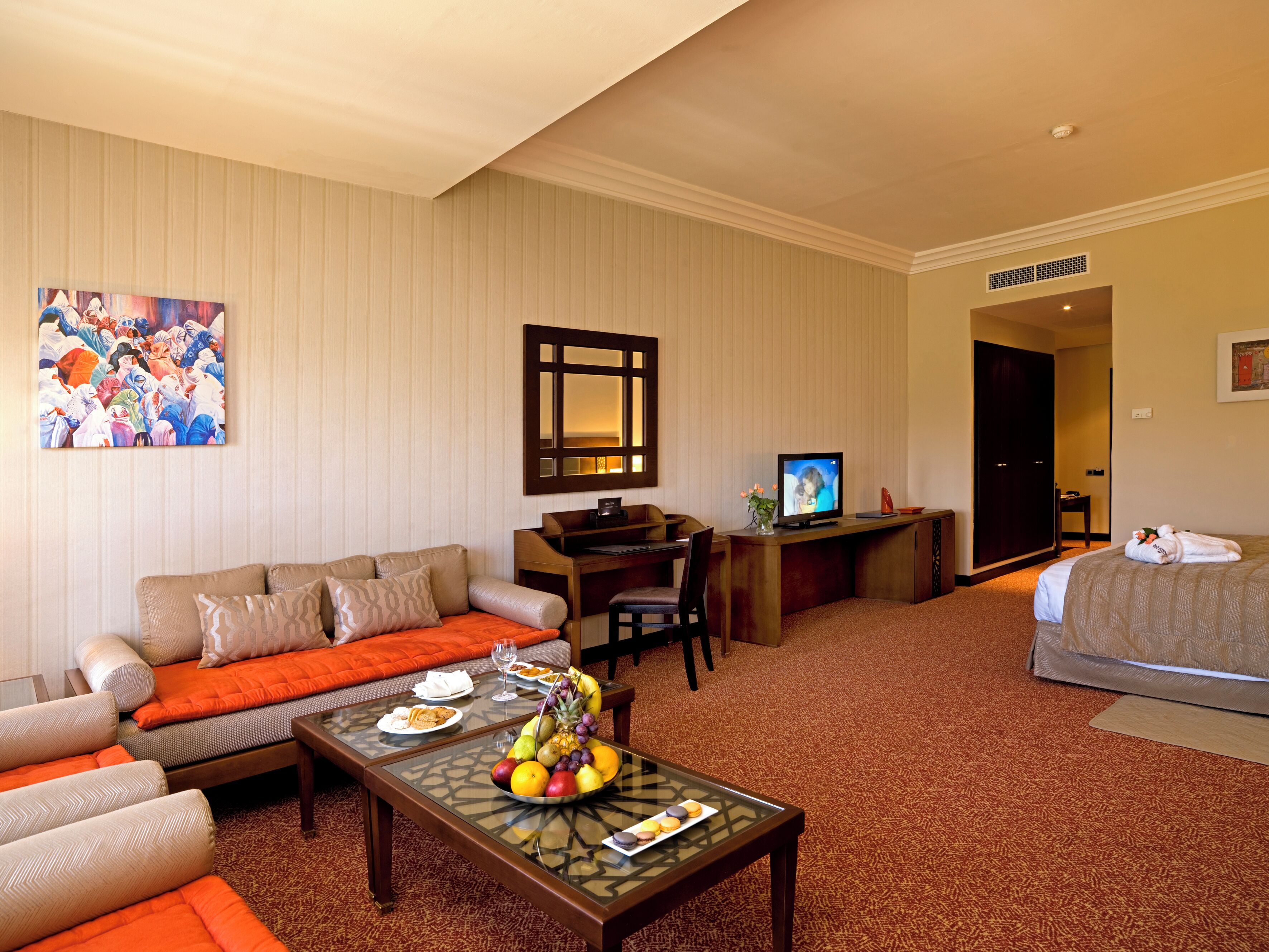 Habitación de hotel con sofá, escritorio, cama y mesa de centro con fruta.
