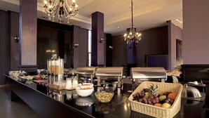 Disposição de buffet com diversos alimentos, uma cesta de frutas e um espaço para café.