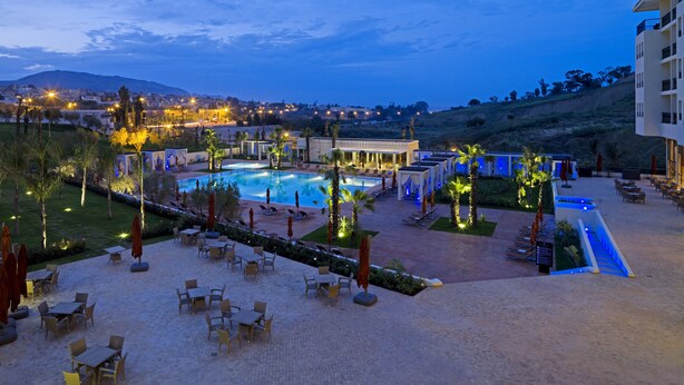 Um resort com piscina, área de estar externa e vista da cidade ao entardecer.