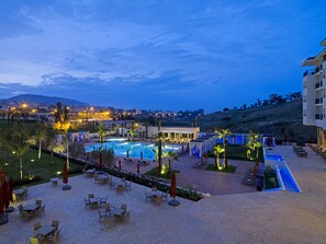 Een resort met een zwembad, terras en uitzicht op de stad in de schemering.