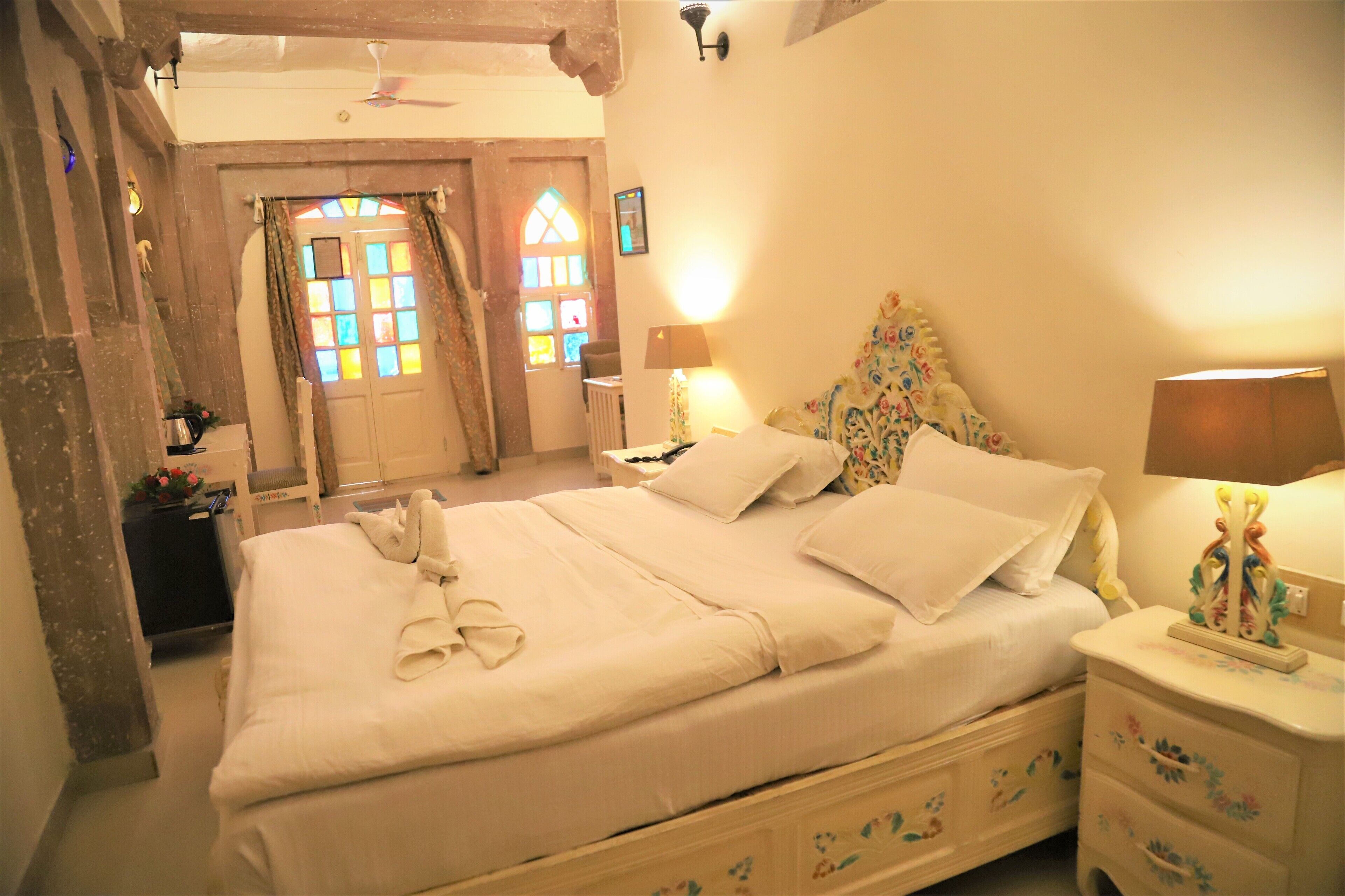 A neatly made bed with pillows and a folded towel, a bedside table with a lamp, and a floral-patterned headboard.