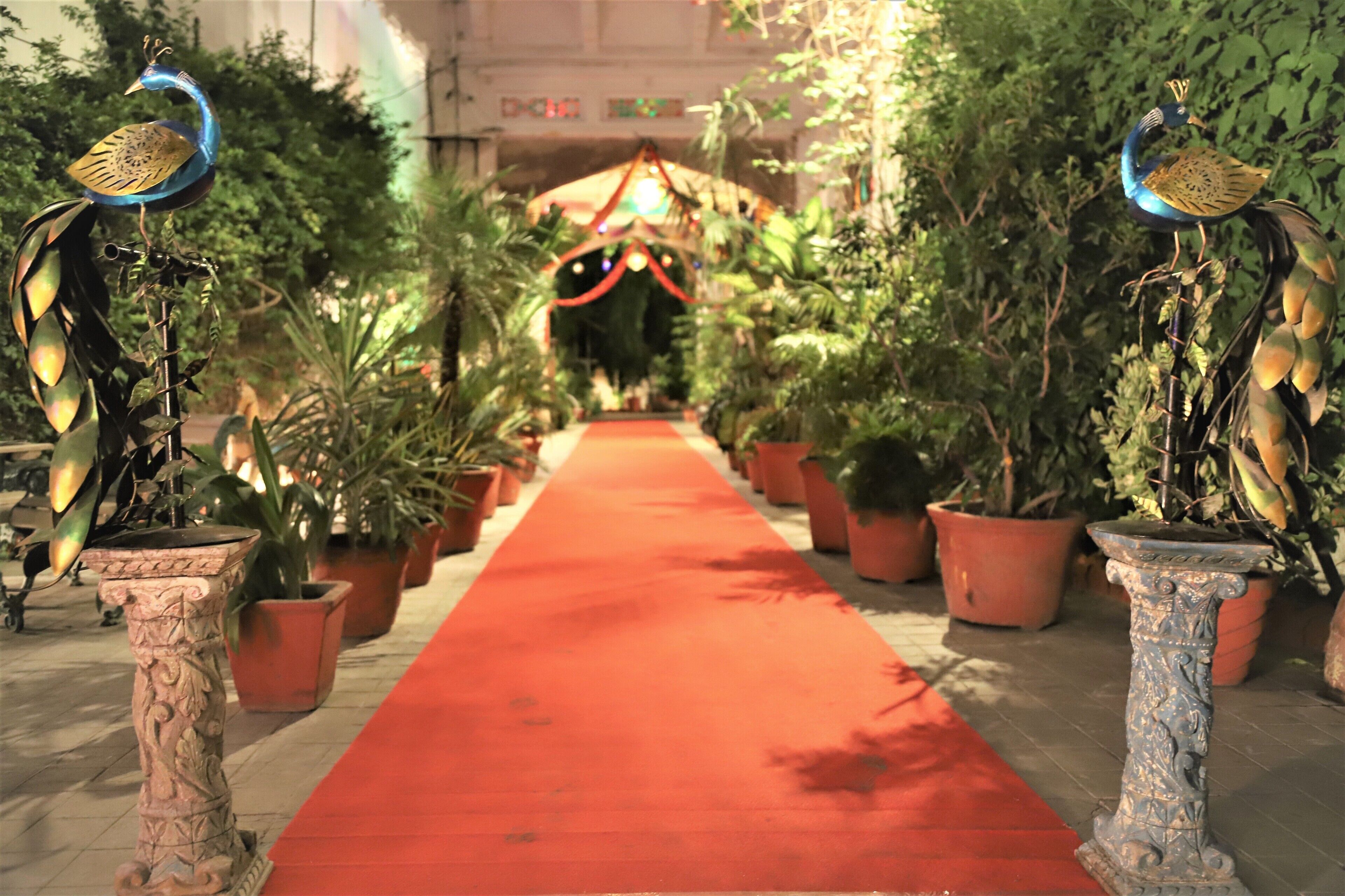 Una alfombra roja conduce a una entrada decorada, con plantas en macetas y dos esculturas de aves a cada lado.