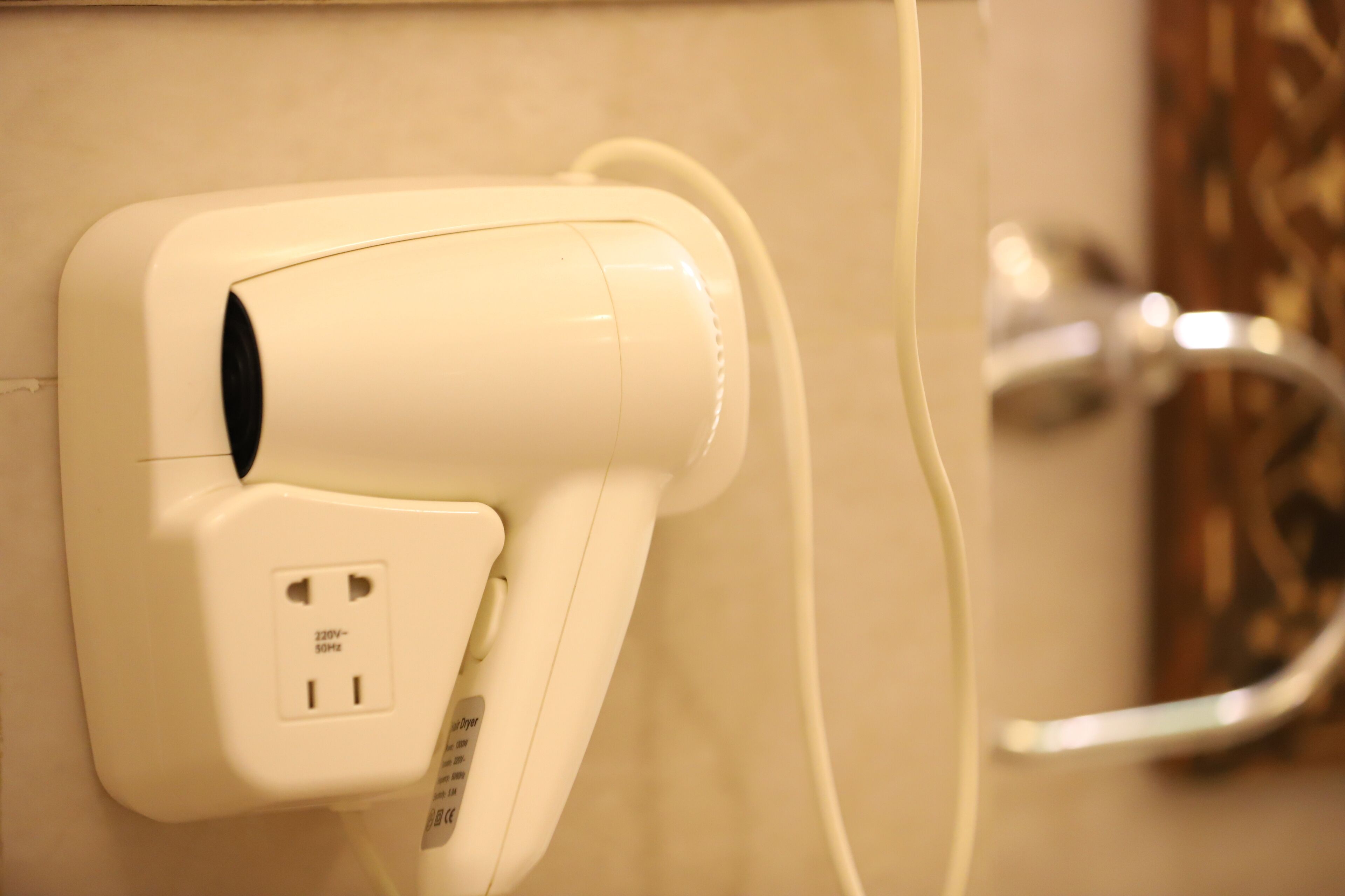 A wall-mounted hair dryer with a power cord plugged into a standard electrical outlet.
