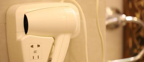 A wall-mounted hair dryer with a power cord plugged into a standard electrical outlet.