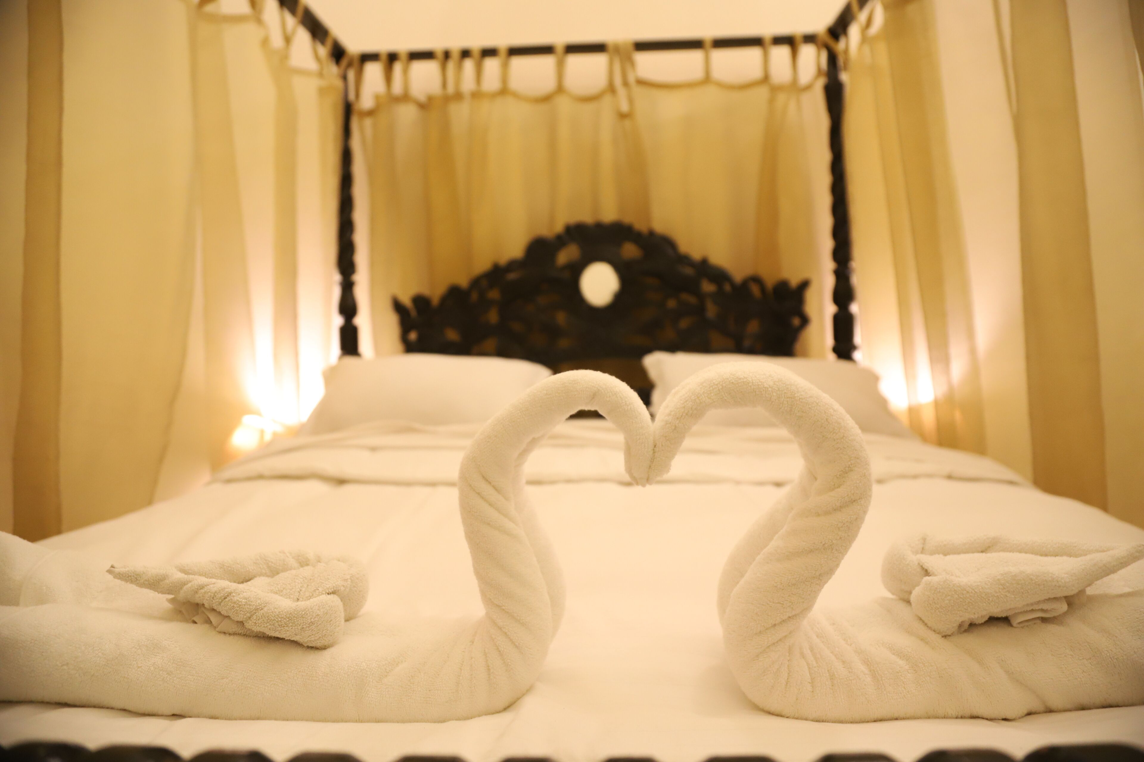 A bed with a canopy and a heart-shaped towel arrangement.