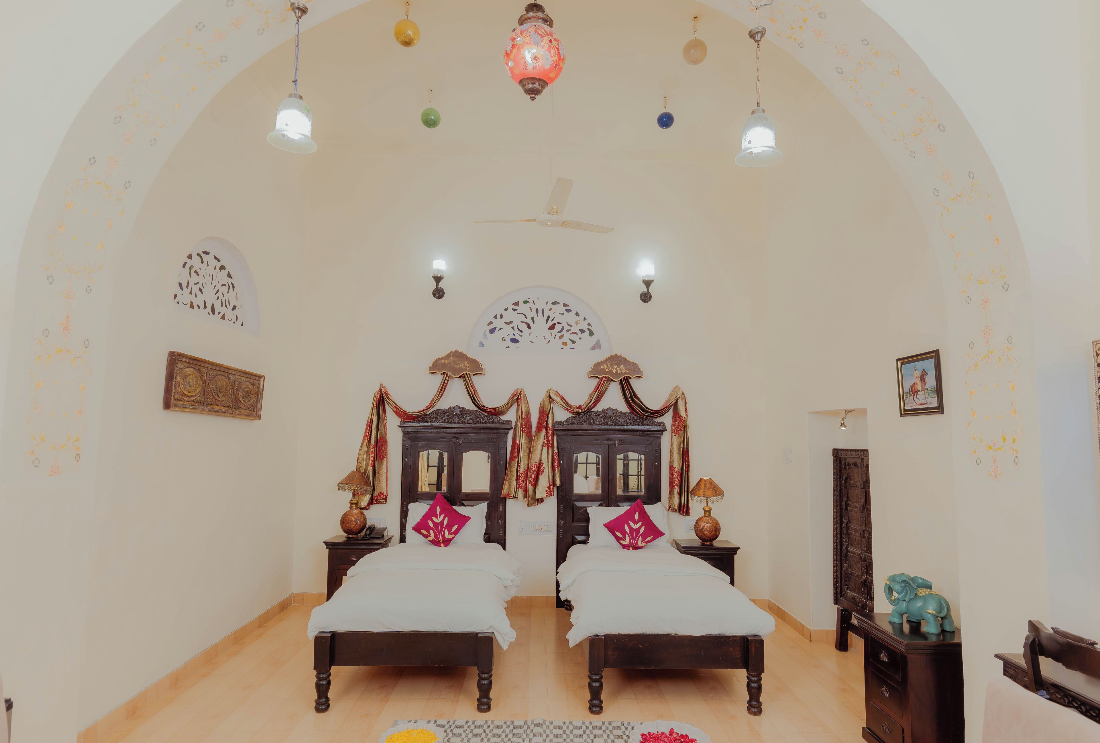 A room with two beds, a ceiling fan, decorative wall sconces, and a large mirror.
