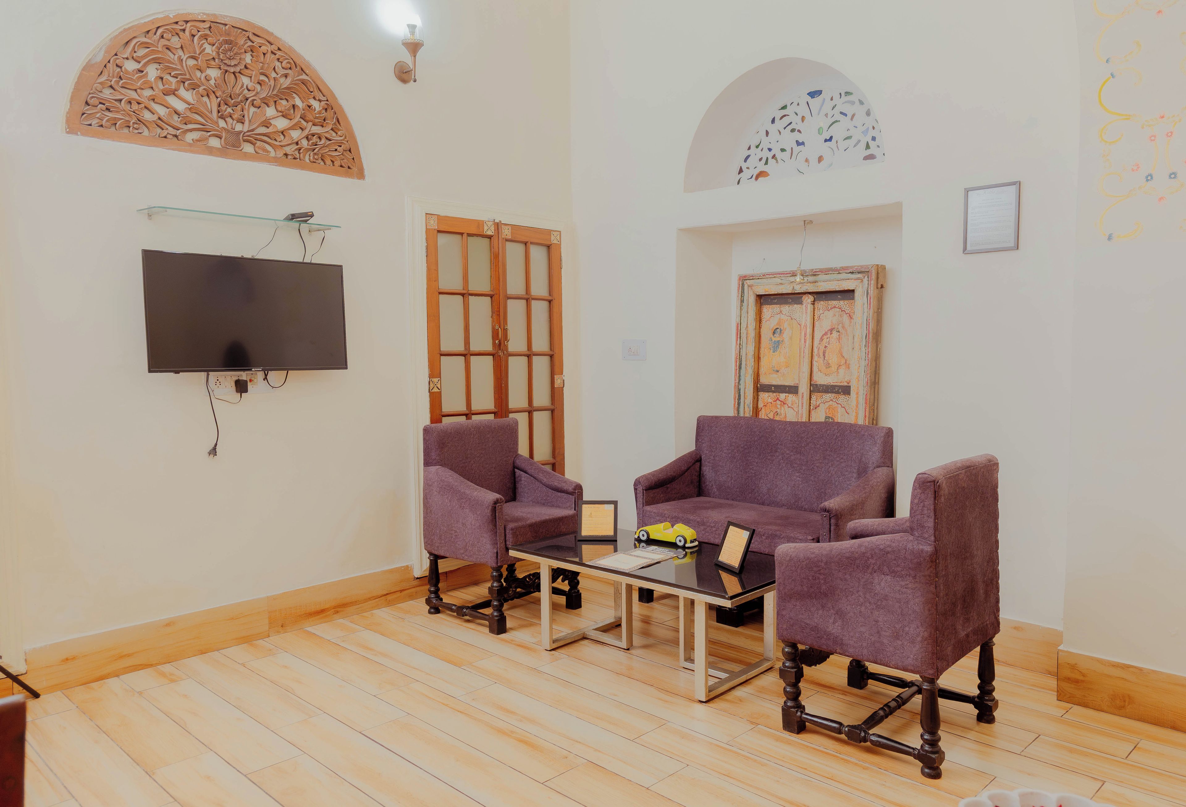 Uma sala de estar com televisão de tela plana, duas poltronas roxas, uma mesa de centro e piso de madeira.