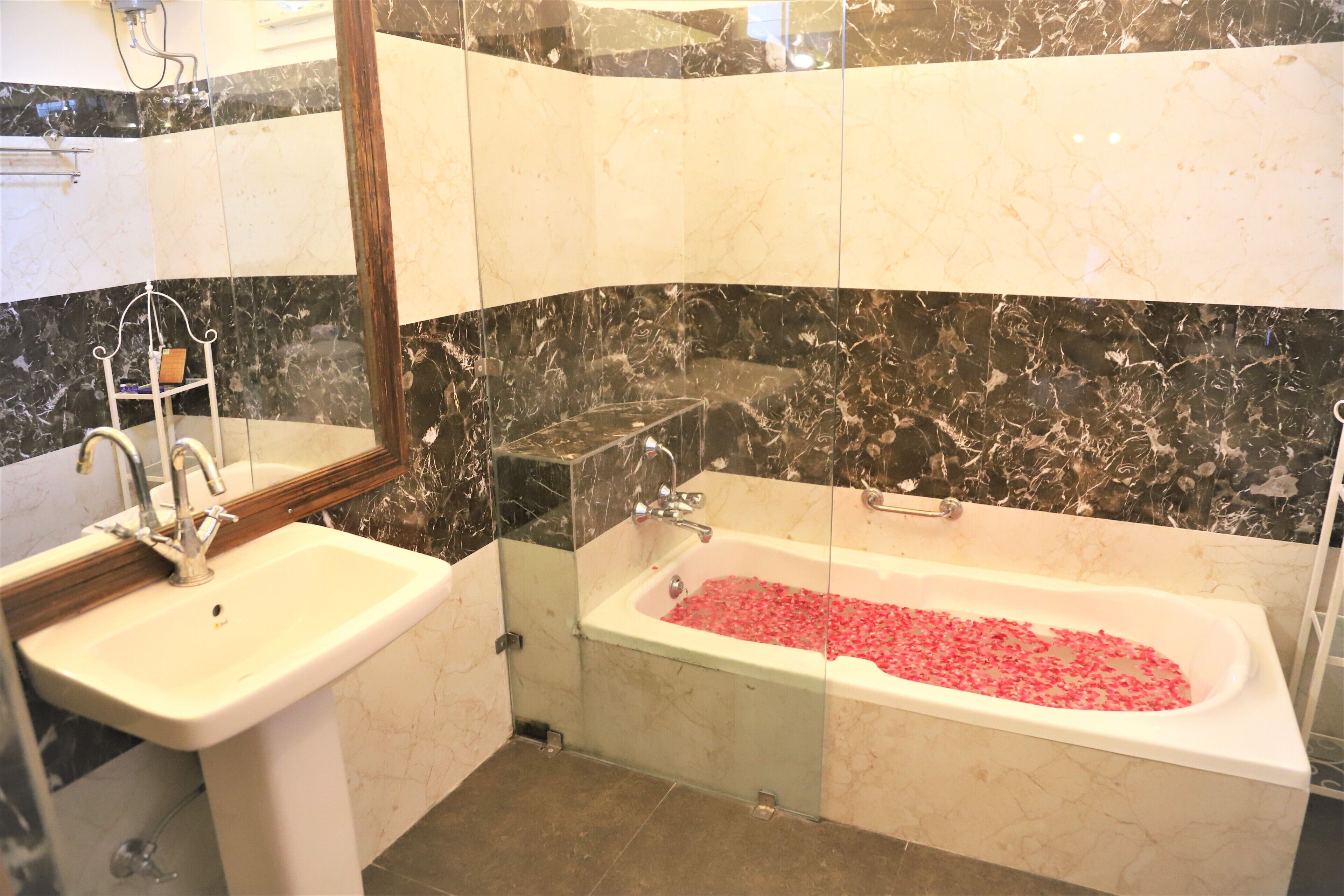 A bathroom with a sink, mirror, and bathtub filled with rose petals.