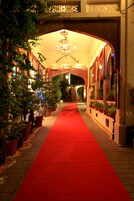 Un pasillo con alfombra roja, plantas en macetas y un candelabro.