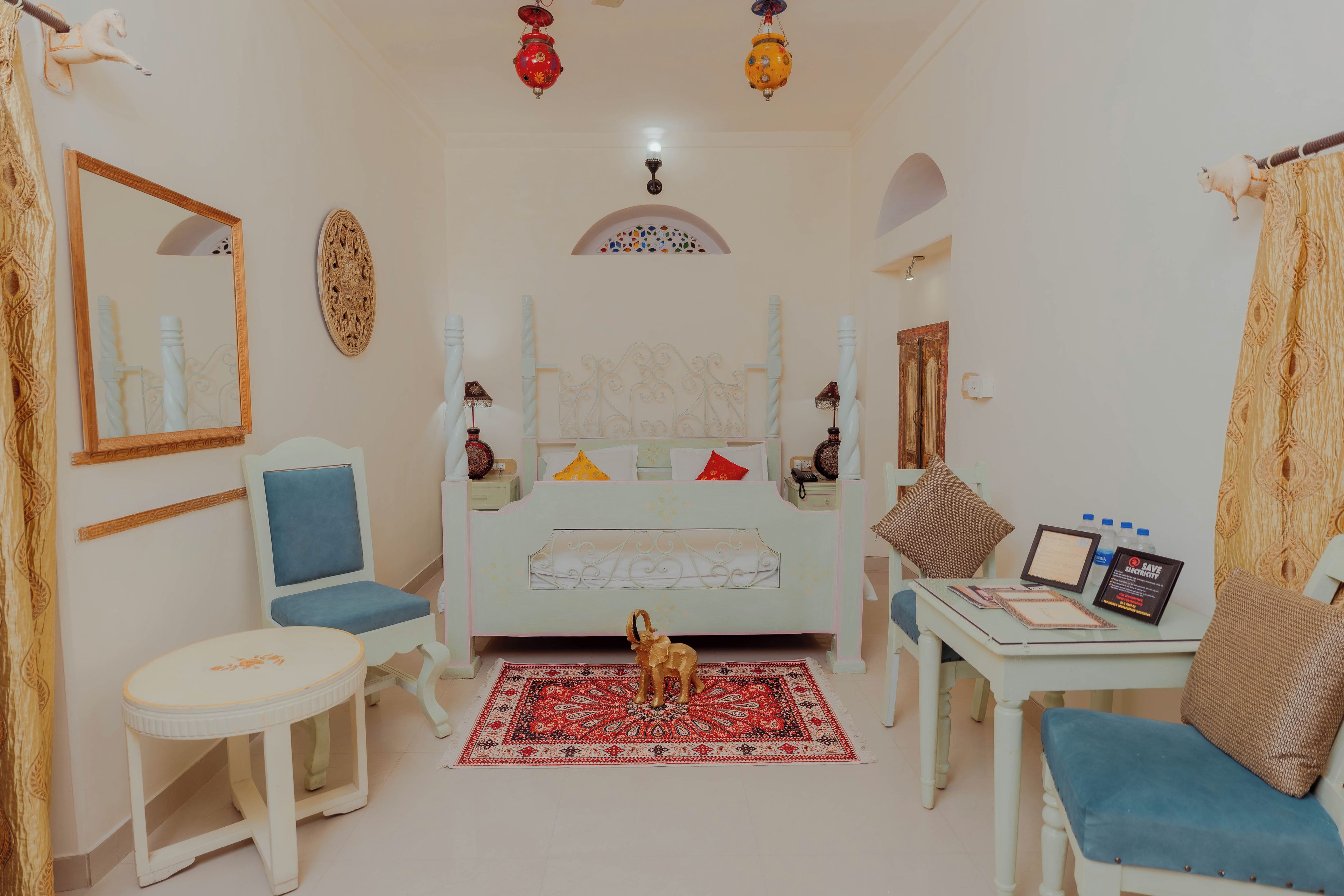 A room with a bed, a desk, a chair, a small table, and a decorative rug.