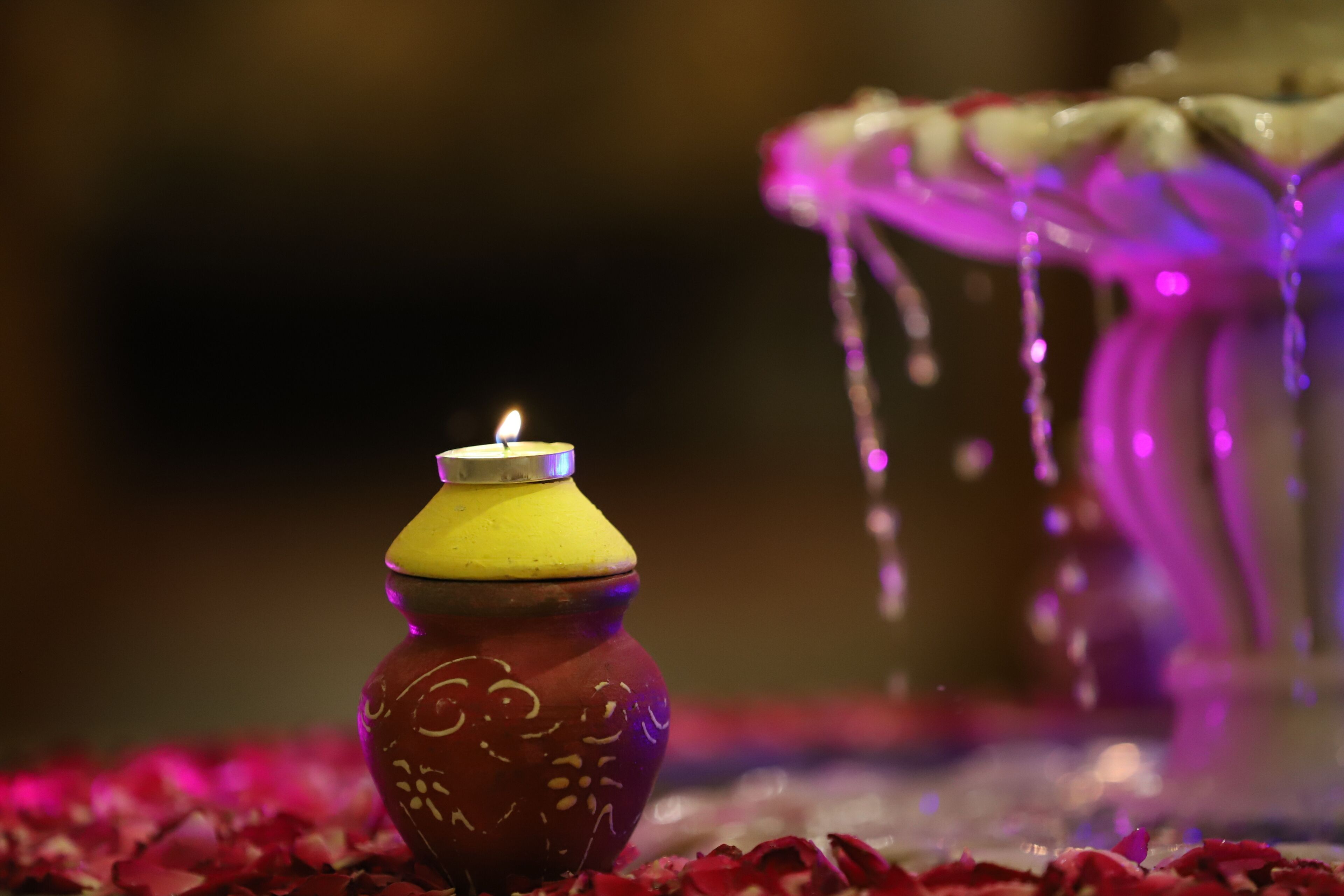A candle in a decorative jar on a bed of rose petals.